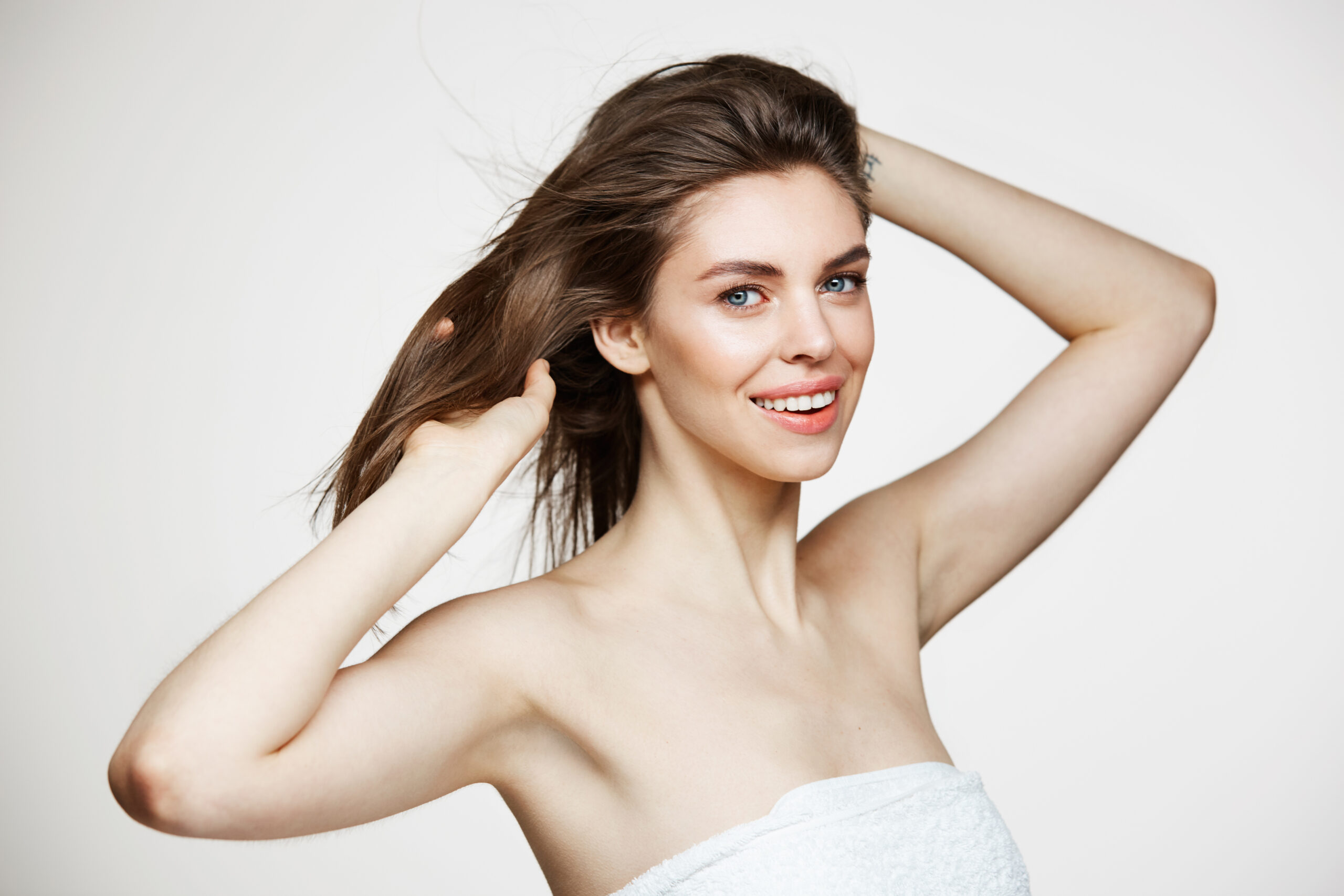 Beautiful Young Girl With Perfect Clean Skin Smiling Looking At Camera Touching Hair Over White Wall Facial Treatment